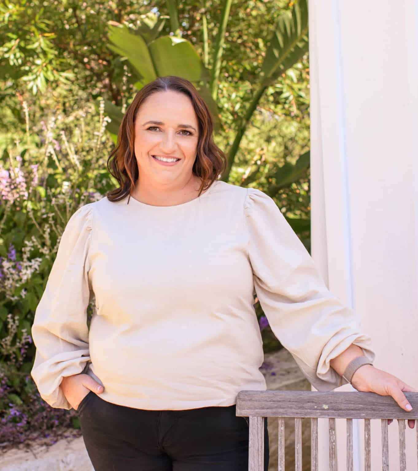 Michelle Gibbons, Clinical Psychologist in the Hawkesbury region. She is wearing a cream coloured top and black pants. She is leaning against the pillar of a wooden deck and has one hand in her pocket.